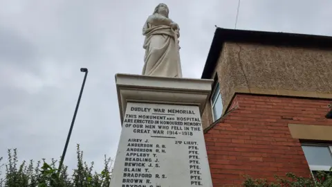 North Tyneside Council The Dudley War Memorial is a white marble plinth with a statue of a woman on top. A list of names is inscribed on the monument, below another inscription that says: "Dudley War Memorial".