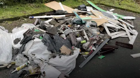 A close-up image of a huge pile of rubbish fly tipped in a layby near Luss - piles of strips of wood and mdf, empty cans and bottles, plastic, chunks of roof tar and general rubbish.