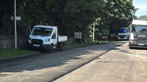 A view of roadworks with half of a road surface removed and vans sitting on top of it