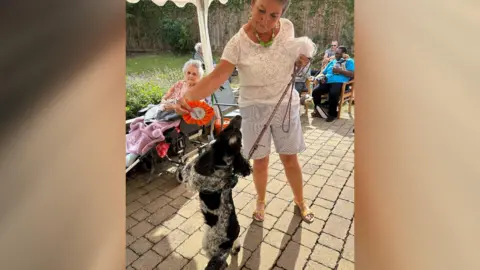 Natalie Crampton A lady holding a rosette for a black dog who is standing up on two legs