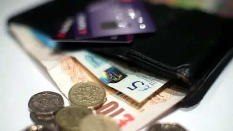 Coins and bank notes spilling out of a black wallet 