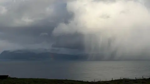South Uist Vibes/BBC Weather Watchers Sleet falls like a white veil from a large white, fluffy cloud over a dark grey area of sea.