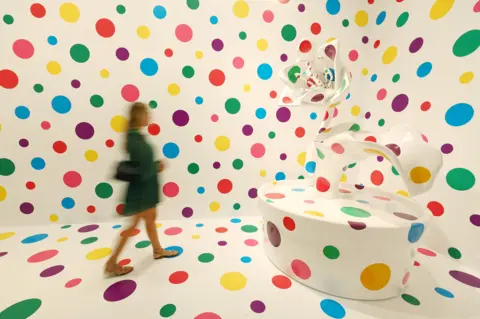 Getty Images A blurred gallery visitor in front of a white wall and sculpture covered in multi-coloured spots