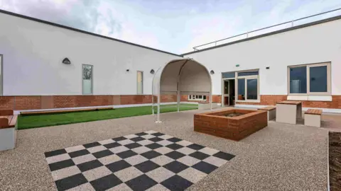 Surrey and Borders Partnership A courtyard area with checkerboards on the floor as well as a small turf grass lawn and seating areas.