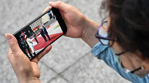 A woman watches a video of US President Donald Trump with China's President Xi Jinping on a mobile phone in Beijing, in May this year