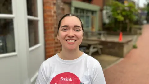 George Carden/BBC Holly Aston outside Java and Jazz Cafe wearing a white t-shirt