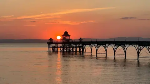 Helen An orange sun is setting behind Clevedon Pier.