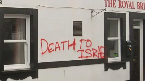Red graffiti reading 'death to Israel' sprayed on a white pub building.
