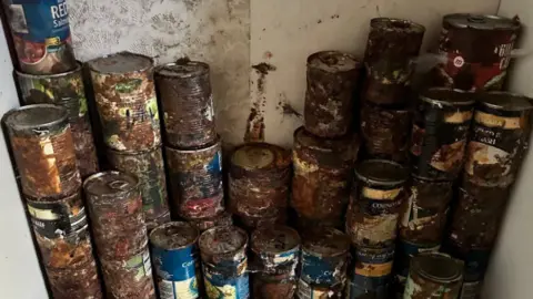 Specialist Cleaning Services A close up of piled up tins of food, which appear to be covered in rust and mould