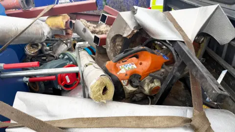 Eddie Mitchell A pile of metal and junk. It includes metal poles, a chainsaw and insulation. 