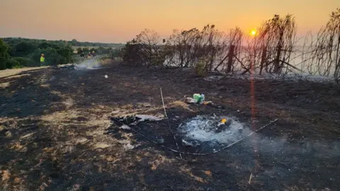 A view of the burned heath land. Some crews are seen around it dampening hotspots.
