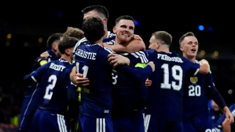 PA Media Players for the Scotland's men's football team hug in their navy football strips on the pitch during the match with Denmark. Andy Robertson can be seen looking emotional.