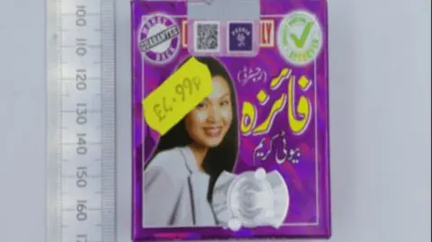 A price tag on a product, with a woman's face on it, with writing in a foreign language. It has a £4.99 yellow price sticker on it. There is also a ruler to the side to show the size to the product. 