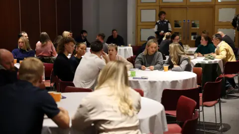 Oxford United A collection of round tables with various people sat around them on red chairs.