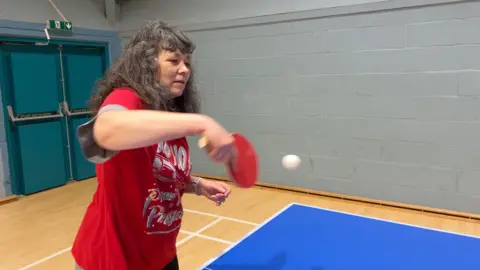 A woman in a red Christmas top returns the ball during a table tennis session organised by Sport in Mind.