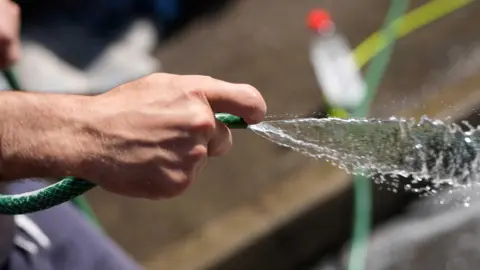 Generic image of a hand holding a hosepipe with water flowing out of it.