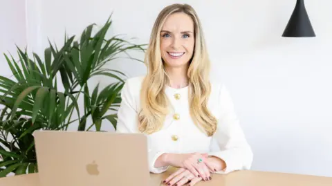 Medi Parry Williams Medi Parry jones is sat at a desk with a laptop in front of her. She is smiling at the camera