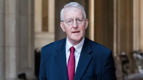Getty Images Hilary Benn speaking. He is wearing a navy suit jacket, white shirt and red tie. He has grey hair and is wearing round glasses.