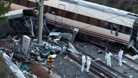 Reuters Um bombeiro e membros da Guarda Civil espanhola trabalham ao lado de um trem envolvido no acidente.