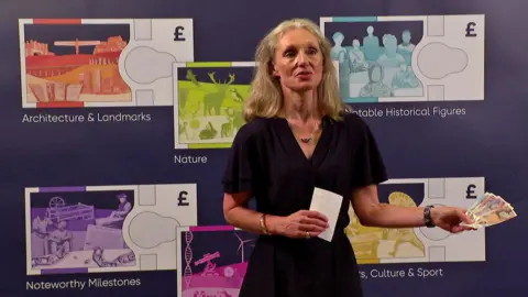 BBC Bank of England chief cashier Victoria Cleland holds banknotes and stands in front of mock-ups of new themed notes.