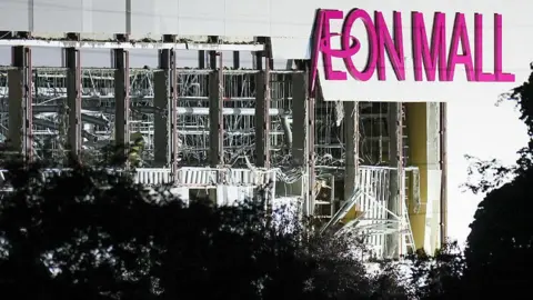 A collapsed shopping mall with a pink sign Aeon Mall on its side.