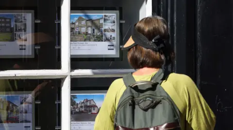 Getty Images A woman with a backpack looks at adverts in the window of an estate agents