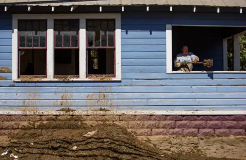 Melissa Sue Gerrits/Getty Images A woman uses a shovel to remove mud from a building on Main Street on October 3, 2024 in Marshall, North Carolina.  