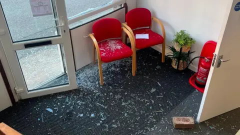 Picture taken inside the donation centre, which can clearly see the brick on the floor. Smashed glass strewn on the dark carpet.
