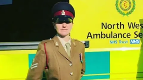 Rachel Claire Lemonofides  is in an amry unform in front of an ambulance with yelow and green livery.