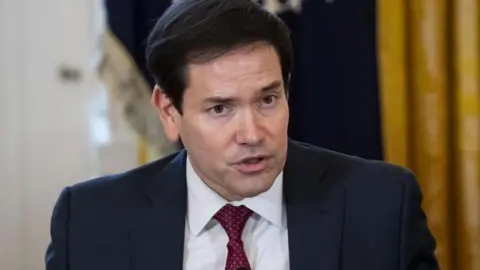 EPA An image of the US Secretary of State, Marco Rubio, speaking into a microphone while wearing a navy suit with a red tie.