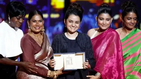 Film director Payal Kapadia holds up an award, surrounded by four other women 