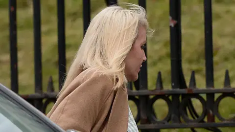 Pacemaker Nichola Hawes pictured outside Downpatrick Court. She is wearing a brown coat and has blonde hair. Behind her is a black fence in front of green grass.