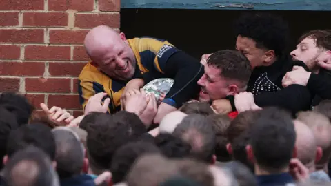 Reuters A man in a yellow top, who had hold of the ball, grimaces as a number of hands try to pry it out of his grasp