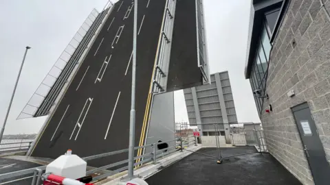 John Fairhall/BBC Herring Bridge in Great Yarmouth is a huge structure, with two wings that are upright to allow ships to pass. Both the road for vehicles and pedestrian pavement across the bridge are at an almost 90 degree angle.