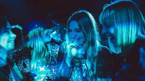 Four women with drinks in their hands, lit by a blue light