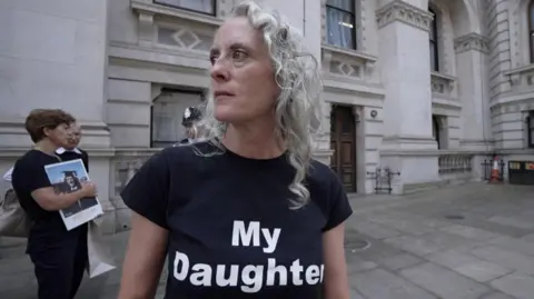 Anne-Marie Cockburn looking off to the side, wearing a black t-shirt that says "My Daughter".