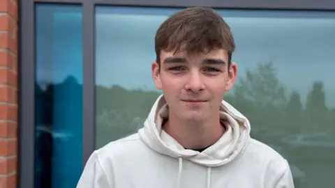 Jack pictured outside, he has short brunette hair and is wearing a white hoodie.