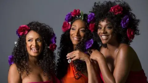 Three women smiling at camera against a plain backdrop.
