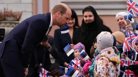 PA Media William is seen bending down to speak with a child who is waving a Union Flag and wearing winter clothes