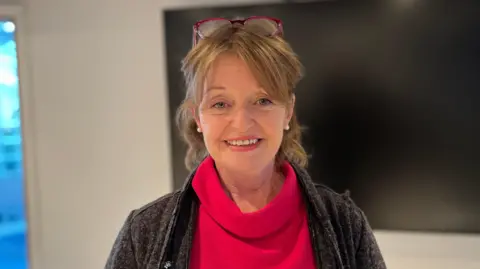 A woman with her glasses on her head in a red, roll-neck jumper and a darker coat