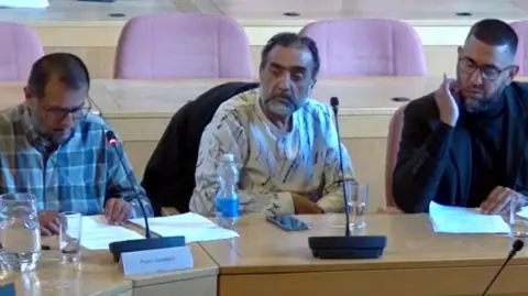 Peterborough City Council Ali Haider wearing a checked shirt, with another taxi driver in white shirt and Zameer Ali wearing a black jacket and black shirt 