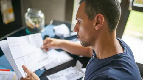 Man looking at paperwork with envelopes in front of him on a desk.