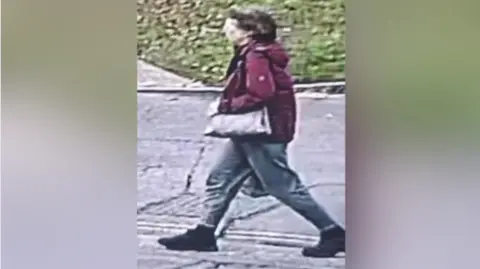 Suffolk Police Christine Murton is pictures on CCTV walking on a road. She is wearing a burgundy coat and grey jeans, with black boots and a bag. She has short brown hair.