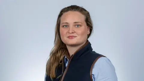 Amy Morris Amy Morris, who has shoulder length brown hair, poses for the camera. She is wearing a light blue shirt and a dark blue gilet