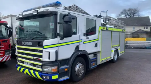 A parked white fire engine with fluorescent green stripes on it 