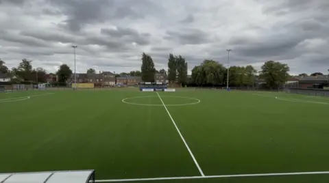 Rob Makepeace, BBC View of the centre of a football pitch, with trees and houses in the background.