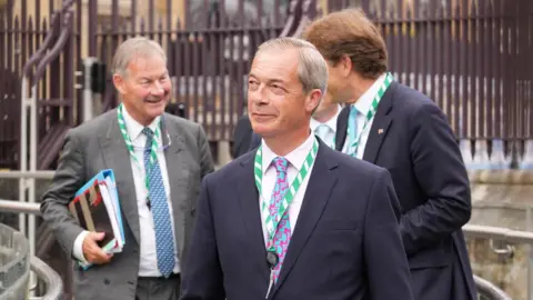 PA Media Nigel Farage and Rupert Lowe outside the Houses of Parliament, with the figure of Richard Tice just behind Farage. All are dressed in smart suits and ties, with Lowe carrying two folders. The picture was taken in July 2024, just after the general election.