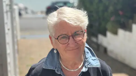 George King/BBC A head and shoulders shot of Kath Gaynor. She is wearing glasses and smiling while looking into the camera.