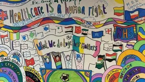 Essex Partnership University NHS Trust A colourful poster that reads 'Healthcare is a human right'. There are flags of different countries and a cartoon drawing  of four people holding a banner that reads 'what we do together matters' 