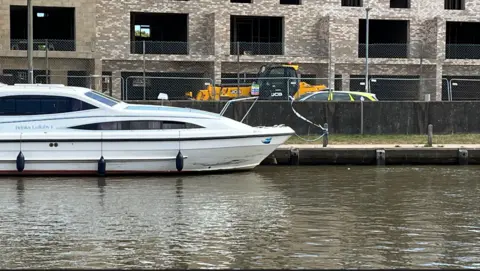 The River Bure at Great Yarmouth with a police cordon near a boat, and a police car parked behind a fence